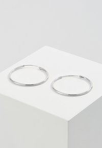 Zilveren oorbellen in de vorm van een gladde, reflecterende ring. Ze zijn cirkelvormig en hebben een dun en minimalistisch ontwerp. Geen zichtbare sluitingen.