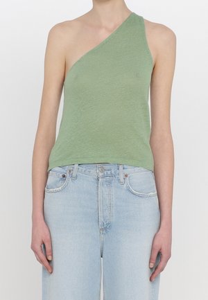 Persoon draagt een lichtgroen one-shoulder mouwloos topje en lichtblauwe hoge taille jeans tegen een egale achtergrond.