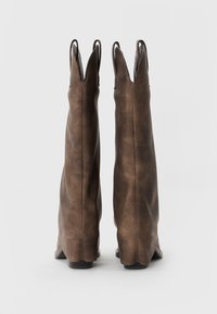 Tall, brown leather boots with pointed tops and textured finish. The sole is black with a slight heel, showcasing a minimalist design.
