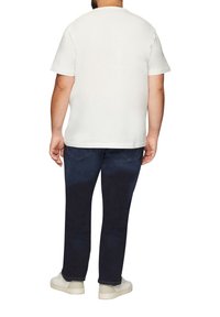 Witte katoenen T-shirt met korte mouwen, gecombineerd met donkerblauwe denim broeken met achterzakken. Model draagt witte sneakers.