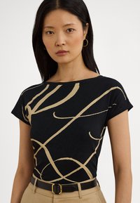 Juoda trumpomis rankovėmis palaidinė su abstrakčiais auksiniais raštais, apvali iškirptė, minkšta medžiaga, derinama su rusvos spalvos diržu ir kelnėmis, akcentuojant spalvų kontrastą.