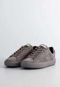 Zapatillas de ante gris con puntera redondeada, diseño de cordones plano y suela de goma. Etiqueta de marca notable en la lengua.