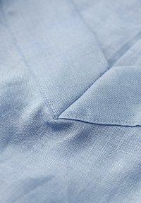 Světle modrá tkanina s texturovanou vazbou, ukazující ohyb rohu s viditelným stehem a hladkým povrchem.