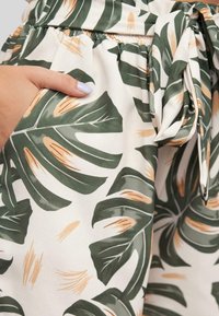 Light-colored shorts featuring a tropical leaf print in green and beige, with an elastic waistband and a tied belt detail.