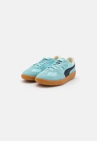 Zapatillas de ante turquesa con un acento azul oscuro, puntera redonda, diseño con cordones y suela de goma. Superficie texturizada y detalle de marca visible.