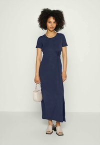 Granatowa sukienka maxi do kolan z krótkimi rękawami i bocznym wiązaniem. Gładka faktura, w połączeniu z lekką torbą i sandałami.
