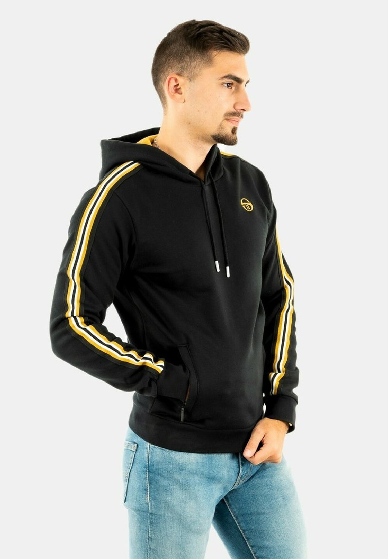 Černá mikina s kapucí s žlutými pruhy na rukávech, klokaní kapsou a stahovací kapucí. Měkká tkanina, atletický střih a logo na hrudi.