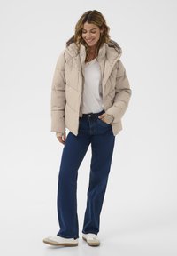 Beige puffatakki, jossa on huppu, ominaisuutena tikkikuviointi ja etuvetoketju. Yhdistetty tummansinisiin suoriin farkkuihin ja valkoisiin lenkkareihin.