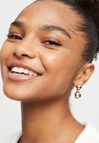 Pendientes de gota de oro con una parte superior circular y una parte inferior ovalada, superficie lisa y acabado reflectante que realza la luz.