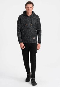 Schwarze, strukturierte Kapuzenjacke mit Kapuze, Kordelzug-Akzenten und einer Fronttasche. Kombiniert mit schwarzen, figurbetonten Cargo-Hosen und schwarzen Sneakern.