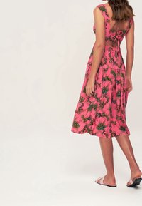 Rotes Kleid mit floralem Muster, ausgestattet mit einem figurbetonten Oberteil, breiten Trägern und einem ausgeschnittenen Rücken. Hergestellt aus leichtem Stoff mit einem fließenden Rock.