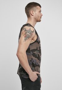 Tricou fără mâneci cu un model camuflaj, cu nuanțe de verde, maro și gri. Materialul pare ușor; designul are brațe largi și o croială lejeră.