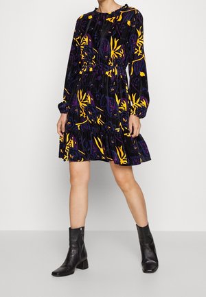 Robe noire à motif floral jaune et violet, avec manches longues, taille élastique et ourlet à volants. Associée à des bottines noires.