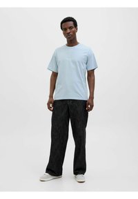 Light blue cotton t-shirt with short sleeves and a crew neckline, featuring a simple text logo. Paired with dark, loose-fitting trousers.