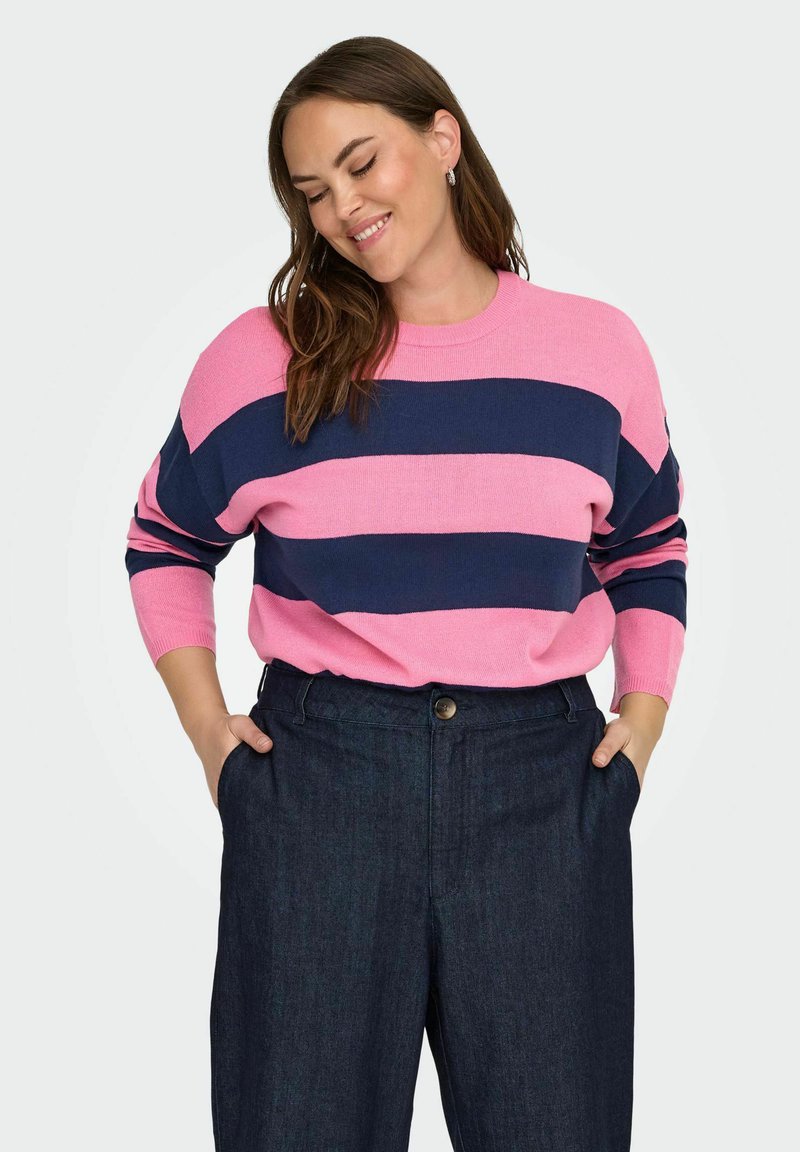 Wzorzysty sweter w różowym i granatowym kolorze, z długimi rękawami i okrągłym dekoltem, zestawiony z ciemnoniebieskimi spodniami dżinsowymi, z zapięciem na guziki.