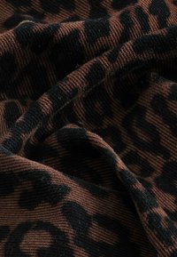 Tissu à motif léopard présentant un schéma de couleurs brun et noir, avec une texture côtelée et des détails de surface doux et duveteux.