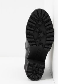 Semelle de bottes en caoutchouc noir présentant un motif antidérapant texturé avec des formes d'étoiles, un bout arrondi, et une finition latérale lisse. Taille 37 embossée.