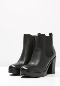 Stivali ankle in pelle nera con punta arrotondata, pannelli laterali elastici e tacco spesso. Texture liscia con una leggera lucentezza.