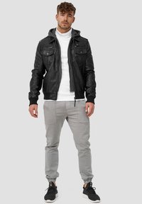 Black leather bomber jacket with a gray hoodie, zippered pockets, and ribbed cuffs, paired with light gray tapered pants and black sneakers.