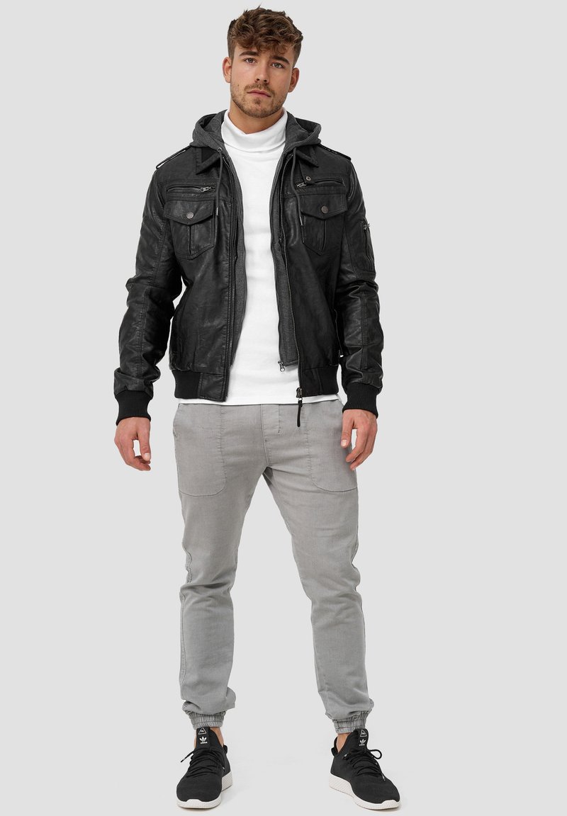 Black leather bomber jacket with a gray hoodie, zippered pockets, and ribbed cuffs, paired with light gray tapered pants and black sneakers.