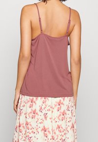 Femme portant un haut sans manches mauve avec des fines bretelles ajustables et une jupe blanche ornée de motifs floraux abstraits roses et violets.