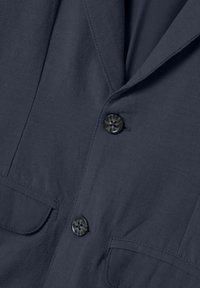 Camicia blu navy con tessuto texturizzato, dotata di due tasche anteriori, chiusura con bottoni e un bottone decorato, e colletto a punta.