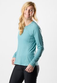 Maglietta sportiva a maniche lunghe blu chiaro con una texture liscia, dotata di scollatura rotonda e vestibilità slim. Indossata con leggings neri.