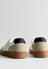 Vita och beige sneakers med svart häl, släta läder- och mockamaterial, rund form, gummisula och perforerade detaljer.