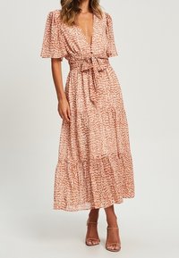 Maximekränning i persikofärgad tyg med en subtil tryck, med en djup V-ringning, korta fladdrande ärmar och ett knytliv. Tierskurt design.