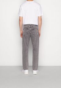 Vaqueros de denim gris con un corte relajado, que presentan una textura deslavada, bolsillos traseros y una etiqueta azul en la cinturilla. Se llevan con una camiseta blanca.