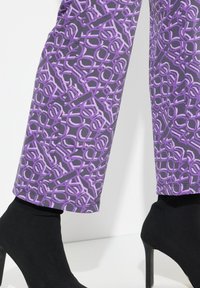 Lilla mønstrede bukser med abstrakte sorte former, parret med sorte højhælede støvler. Materialet ser glat ud med et tætsiddende design.