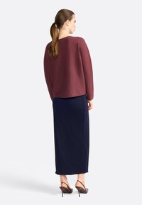 Haut bordeaux à manches longues avec une coupe ample, associé à une jupe maxi bleu marine. Des chaussures à talons bruns complètent l'ensemble.