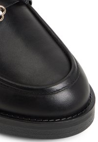 Černá kožená bota s zaoblenou špičkou, jemným vyšíváním a texturovanou černou podrážkou. Obsahuje dekorativní stříbrný kovový detail.