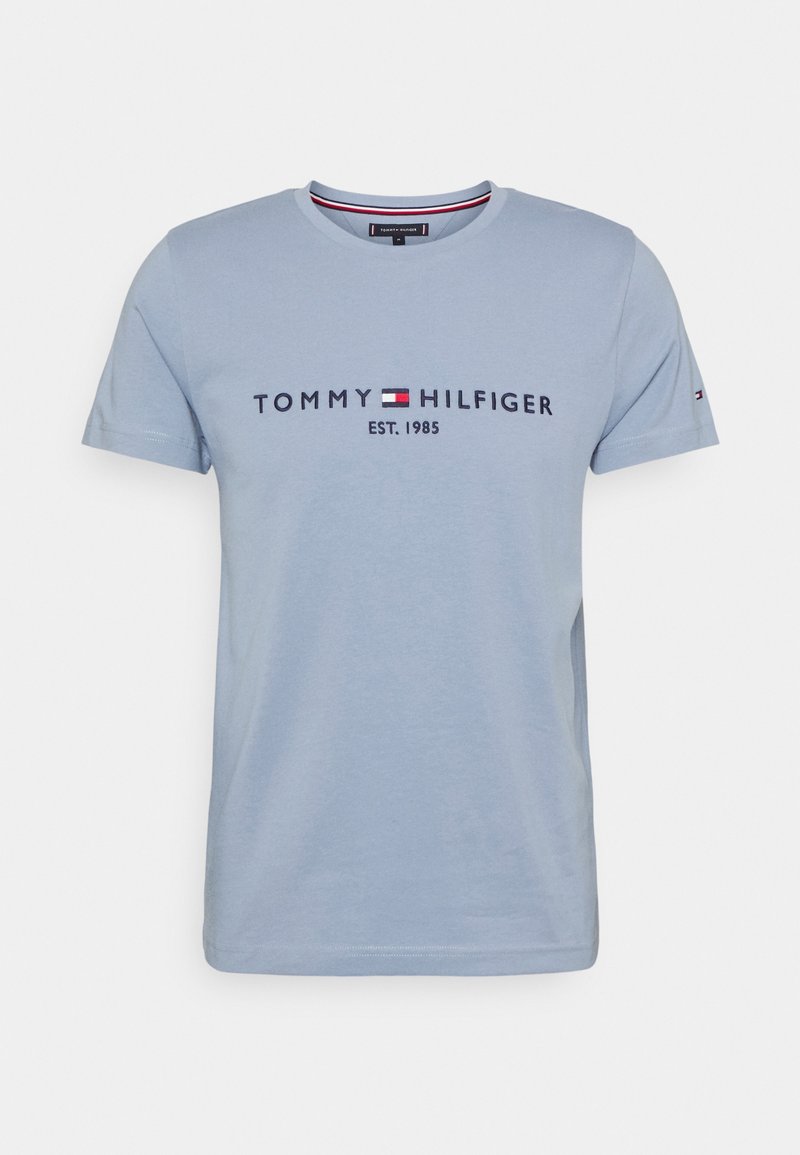Camiseta de algodón azul claro con mangas cortas, cuello redondo y estampado en el frente que dice "TOMMY HILFIGER EST. 1985" con acentos en azul marino y rojo.