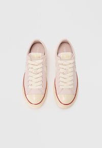 Sneakers in tela rosa chiaro con accessori crema e una punta lucida rosa pallido. Lacci beige, bordatura rossa e suola in gomma color beige.