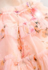 Lyserød tyllkjole med flæselag og blomsterprint i pastelfarver. Glitrende detaljer fremhæver det lette, gennemsigtige materiale.