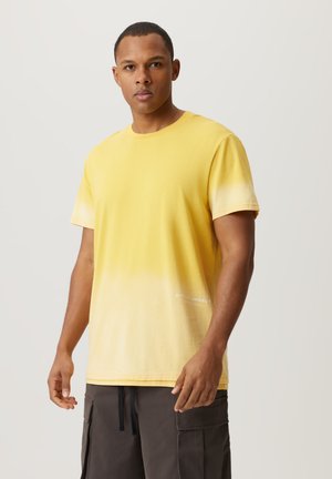 Żółta bawełniana koszulka z gradientowym wzorem, który przechodzi w biel na dolnej krawędzi, z napisem "CITY OF ANGELS" wydrukowanym na białym tle w pobliżu dołu.