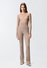 Bež majica dugih rukava od rebrastog pletiva uparen s odgovarajućim visokim, raširenim hlačama. Srebrne, zaobljene balerinke upotpunjuju odijelo.