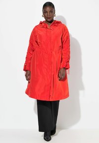Manteau rouge, léger, résistant à l'eau, avec une capuche, des manches froncées et une taille cintrée. Équipé de fermetures éclair métalliques et d'une coupe décontractée.