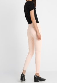 Jeans skinny de color rosa claro con dobladillo desflecado, combinados con una camiseta negra ajustada y zapatos de tacón bloque negro. Tejido suave con un ajuste ceñido.