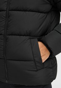Black puffer jacket with a quilted design, featuring a zipper and side pocket. The texture is smooth and slightly glossy.