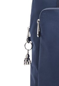 Bolso de tela azul marino con una textura suave, que presenta un zipper plateado y un charm de una pequeña figura colgando de un llavero.