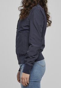 Navy bomber jacket in smooth fabric, zipper front, side pockets, ribbed cuffs, and hem. Features a fitted design with a casual silhouette.