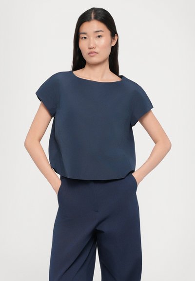 Bluză scurtă de culoare albastru marin, cu mâneci scurte, având un guler rotund larg și un material neted, ușor. Asortată cu pantaloni matching.