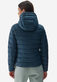 Niebieska, puszysta kurtka z poziomym pikowaniem i kapturem. Wykonana z błyszczącego, ocieplonego materiału, ma dopasowany krój i elastyczne mankiety.