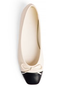 Ballerines en cuir synthétique crème avec un embout en cuir verni noir, dotées d'un nœud décoratif à l'avant et d'une doublure intérieure lisse.
