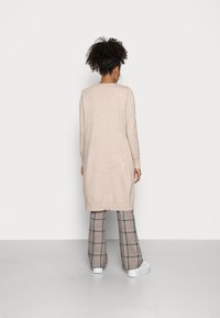 Beige Strickkleid mit langen Ärmeln und geradem Schnitt, kombiniert mit karierter, weit geschnittener Hose in Schwarz, Beige und Rot. Weiße Sneakers.