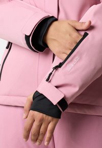 Giacca rosa con dettagli neri, dotata di tasca con zip sul braccio e chiusura in velcro al polso. Texture liscia, vestibilità su misura.