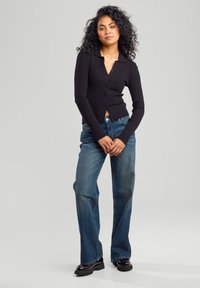 Black ribbed button-up cardigan with a collared neckline, worn over light blue wide-leg jeans and black platform shoes.