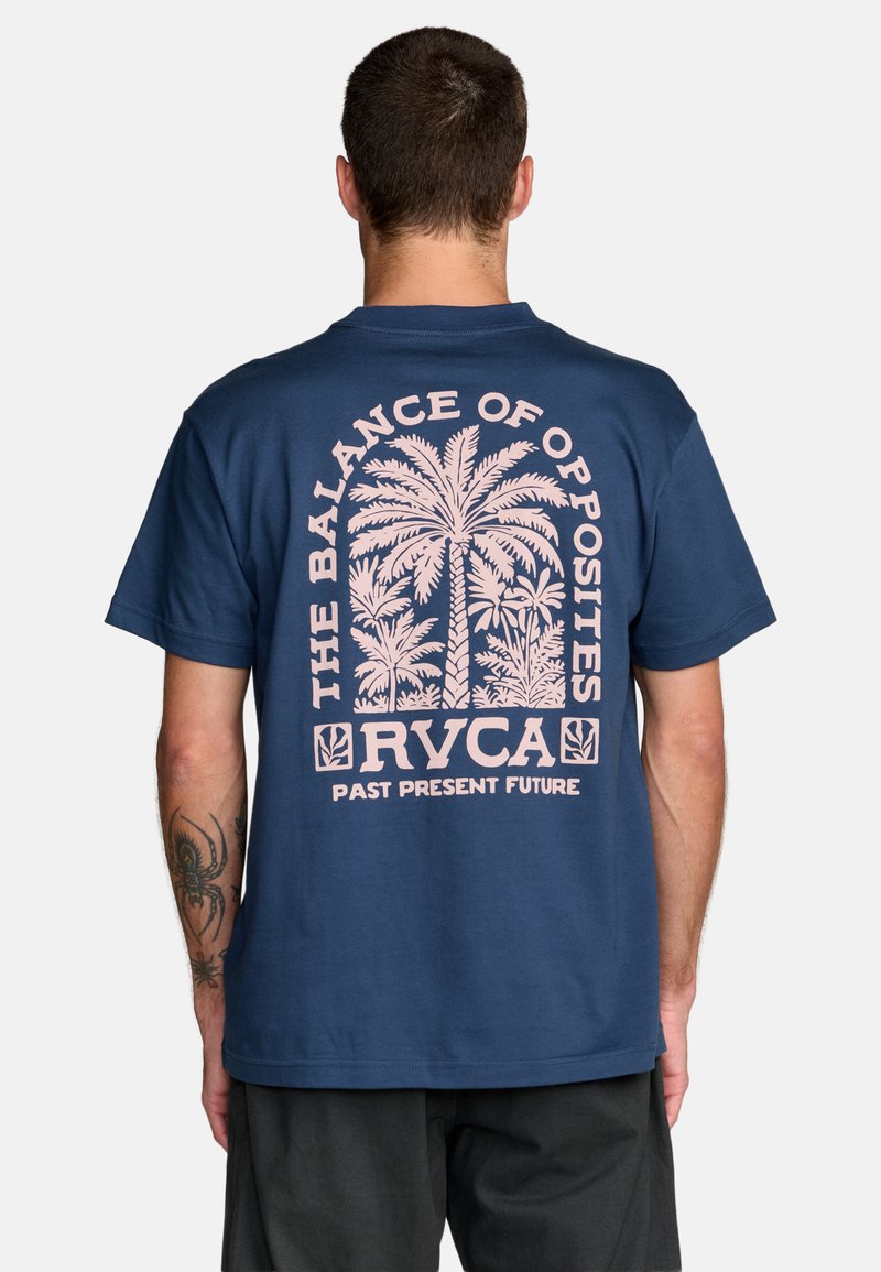 Mann trägt ein marineblaues T-Shirt mit einem pinken Palmenmotiv und dem Text "The Balance of Opposites RVCA Past Present Future" auf dem Rücken.